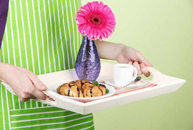 Frau in grüner Schürze mit Holztablett mit Frühstück, auf Farbwand