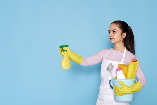 Frau in Gummihandschuhen und sauberer Schürze mit Eimer mit Reinigungsmitteln