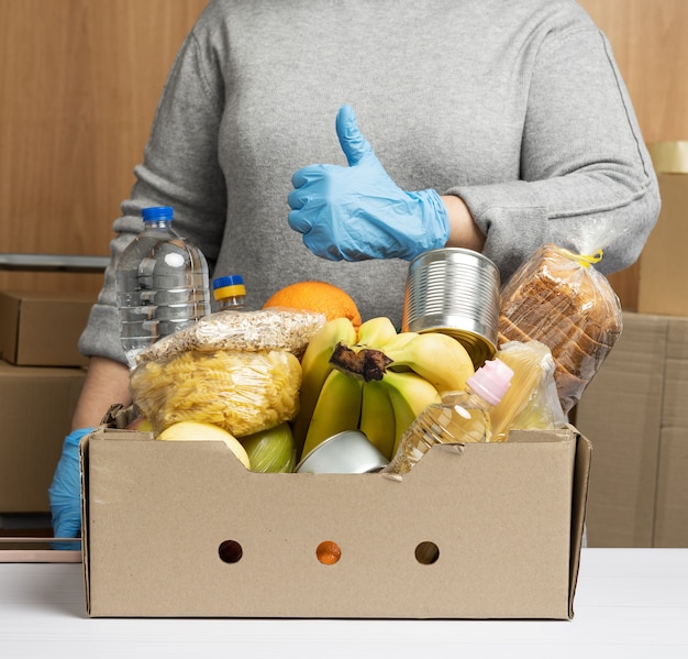 Frau in Handschuhen sammelt ständig Lebensmittel, Obst und Dinge sowie einen Karton, um den Bedürftigen, dem Konzept der Hilfe und der Freiwilligenarbeit zu helfen.