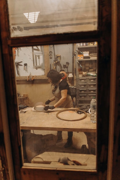 Frau in Handwerkswerkstatt, die mit Holzblick aus einem Fenster arbeitet