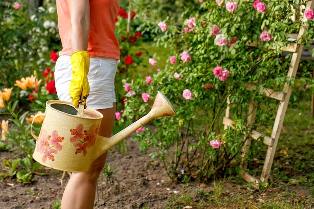 Frau in Haushaltshandschuhen mit einer Gießkanne im Garten zwischen den Blumen