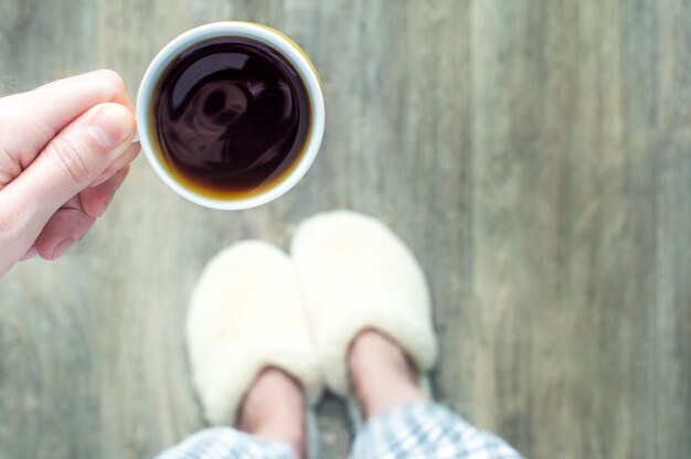 Frau in Hausschuhen hält eine Tasse Kaffee in ihren Händen.