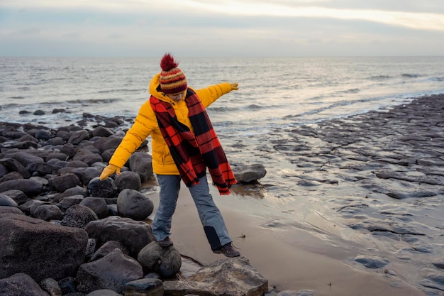 Frau in hellgelber Jacke, die an kalten Wintertagen allein am Meer spazieren geht Travel Lifestyle-Konzept