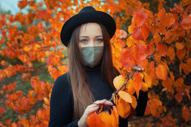 Frau in Hut und Maske über einem Herbstbaum