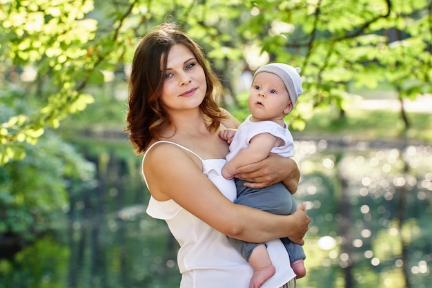 Frau in ihrem s mit Baby in ihren Armen geht im öffentlichen Park des Sommers