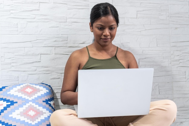 Frau in ihren 3039ern, die zu Hause an ihrem Laptop arbeitet und auf dem Boden sitzt