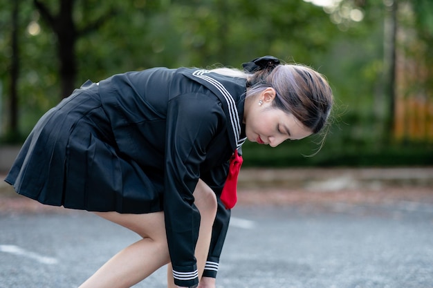 Frau in japanischer Schuluniform im Park kniet im Freien und bindet Schnürsenkel