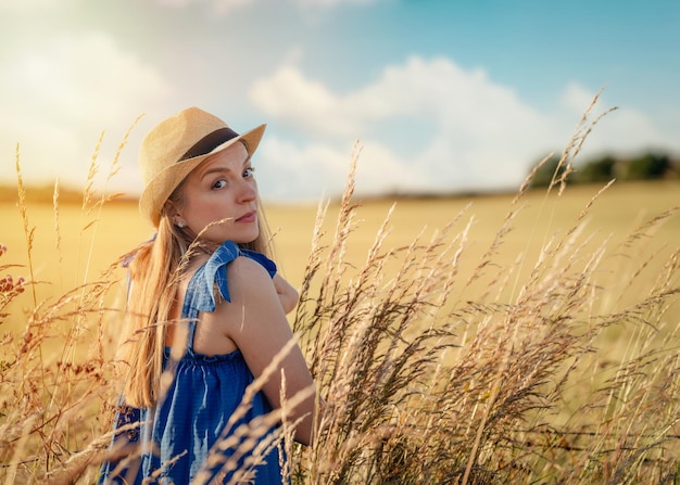 Frau in Kleid und Hut, die im Sommer auf einem Weizenfeld spazieren geht