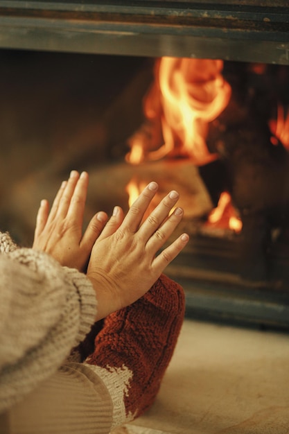 Frau in kuscheligen Socken wärmt Füße und Hände am Kamin auf Heizhaus mit Holzofen