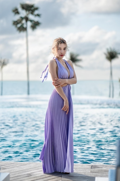 Frau in lila Kleid posiert am Pool mit Meerblick.