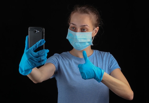 Frau in medizinischen Handschuhen und Gesichtsmaske macht Selfie am Telefon.