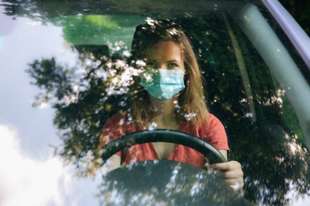 Foto frau in medizinischer maske fährt das auto. coronavirus-zeit. gefährliche situation.