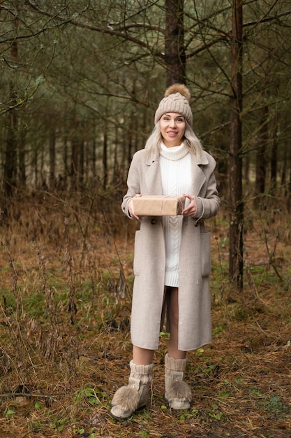 Frau in Mode warme Kleidung mit Geschenkbox in Kraftpapierverpackung auf Naturhintergrund