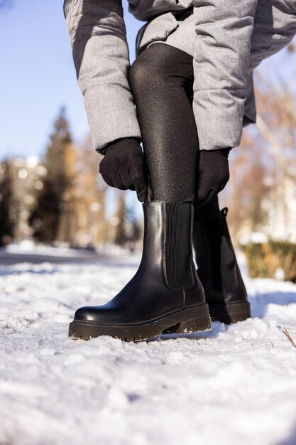 Frau in modischen schwarzen Stiefeln auf weißem Schnee Nahaufnahme Damenbeine in stilvollen Winterlederstiefeln