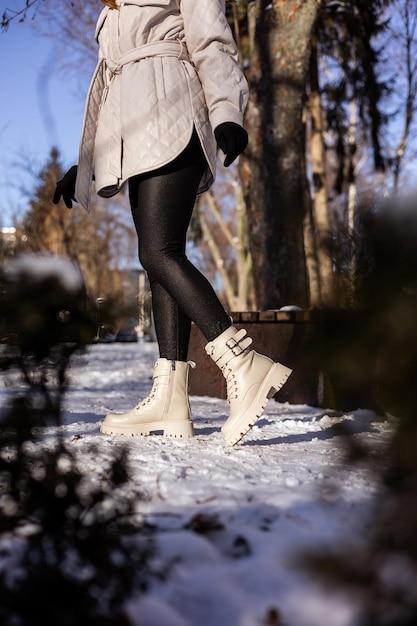 Frau in modischen weißen Stiefeln auf weißem Schnee Nahaufnahme Frauenbeine in stilvollen Winterlederstiefeln