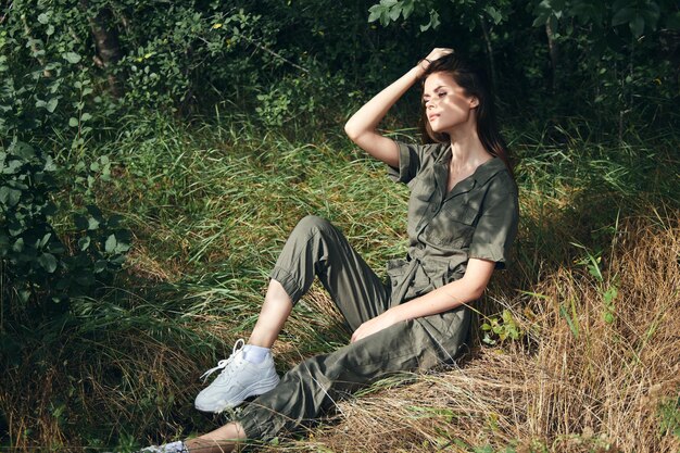 Foto frau in overalls entfernt hübsche haare von ihrem gesicht und sitzt auf dem gras im wald