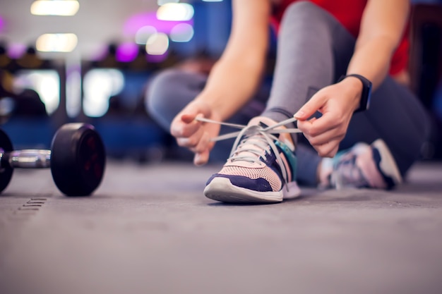 Frau in rotem Top mit kurzen blonden Haaren, die vor dem Training im Fitnessstudio Schnürsenkel binden. Menschen-, Fitness- und Lifestyle-Konzept