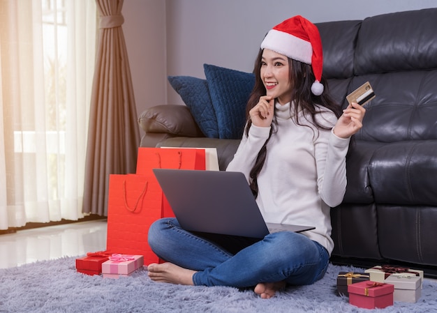 Frau in Sankt-Hut denkend an online kaufen für Weihnachtsgeschenk mit Laptop im Wohnzimmer