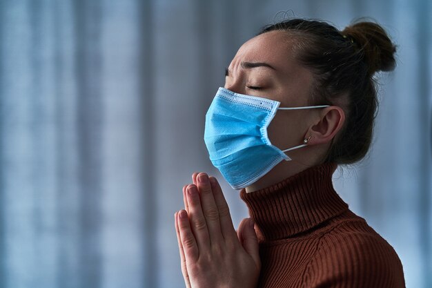 Frau in schützender Gesichtsmaske mit geschlossenen Augen und betenden Händen