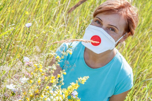 Frau in Schutzmaske, die einen Strauß Wildblumen hält und versucht, Allergien gegen Pollen zu bekämpfen.
