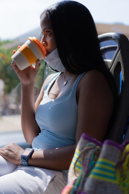 Frau in Schutzmaske, die während der Pandemie Kaffee in einem Bus trinkt