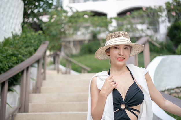 Frau in schwarzem Kleid und Strohhut, die auf einem tropischen Gartenresort spaziert.