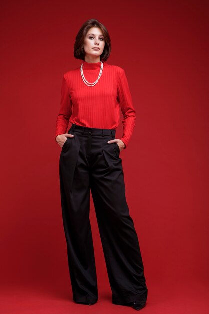 Frau in schwarzer Hose rotes Top Perlenkette auf rotem Hintergrund Bob Haarschnitt Studio Shot