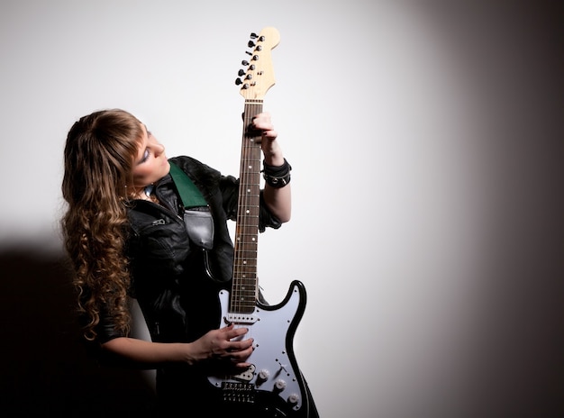 Foto frau in schwarzer lederkleidung, hockt und umklammert ihre gitarre. kopf zur seite gedreht
