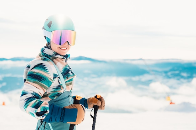 Foto frau in skikleidung mit helm und skibrille auf dem kopf mit skistöcken winterwetter auf der piste berg und blick genießen alpiner skifahrer wintersport skitouren