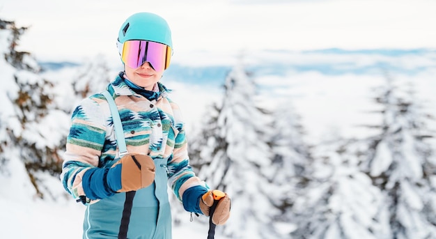 Frau in Skikleidung mit Helm und Skibrille auf dem Kopf mit Skistöcken Winterwetter auf der Piste Oben auf einem Berg und Blick genießen Alpiner Skifahrer Wintersport