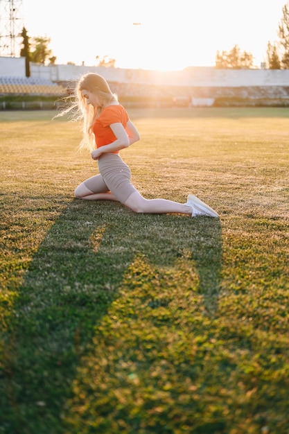 Frau in Sportbekleidung beim Stretching auf Gras Mädchen trainiert Mädchen im Frontallicht