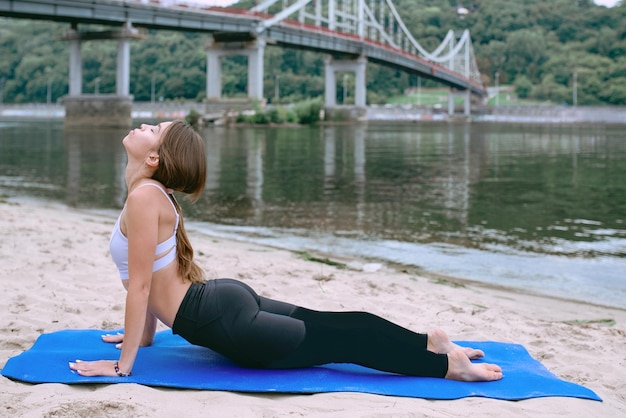 Frau in Sportbekleidung in verschiedenen Yoga-Asanas im Freien am Strand am Fluss