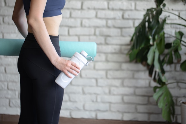 Frau in Sportbekleidung mit Sportgeräten und Thermosflasche nach einem Training im Fitnessstudio. Sport und gesundes Lifestyle-Konzept.