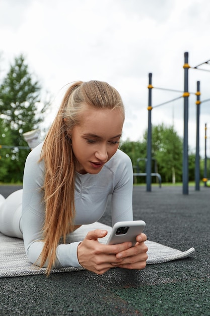 Frau in Sportkleidung, die im Park auf ihr Handy schaut