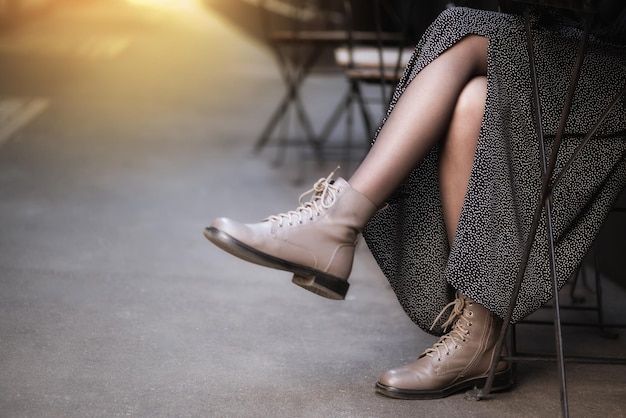 Frau in stylischem Rock und Lederstiefeln sitzt im Straßencafé