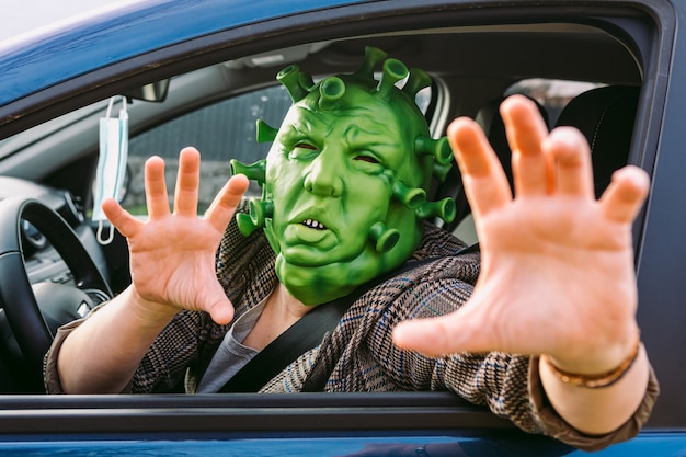 Frau in Verkleidung - Coronavirus-Covid-19-Maske, die ein Auto fährt, aus dem Fenster späht und Angst macht