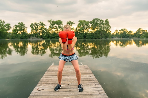 Frau in Verteidigungsstellung mit Boxhandschuhen Outdoor-Training auf dem See bei Sonnenuntergang