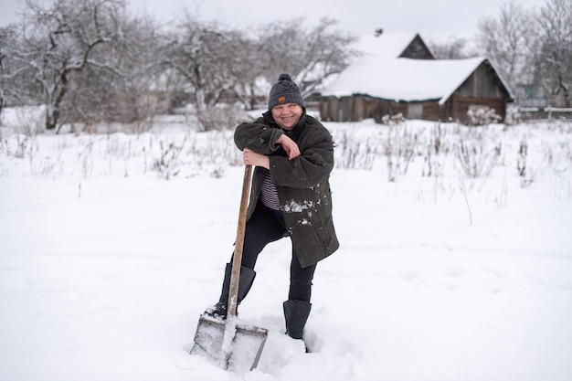 Frau in warmer Kleidung mit Schaufel entfernt Schnee vom Hof