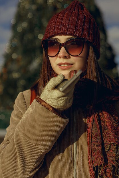 Frau in warmer Oberbekleidung und Sonnenbrille, die Sprachnachrichten auf dem Smartphone aufzeichnet