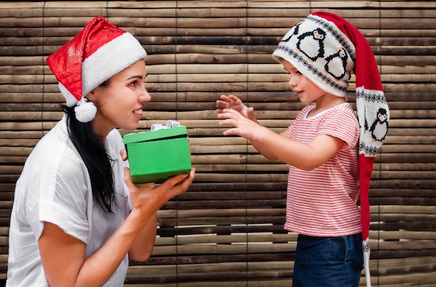 Frau in Weihnachtsmütze hält einem Kind eine Geschenkbox hin.