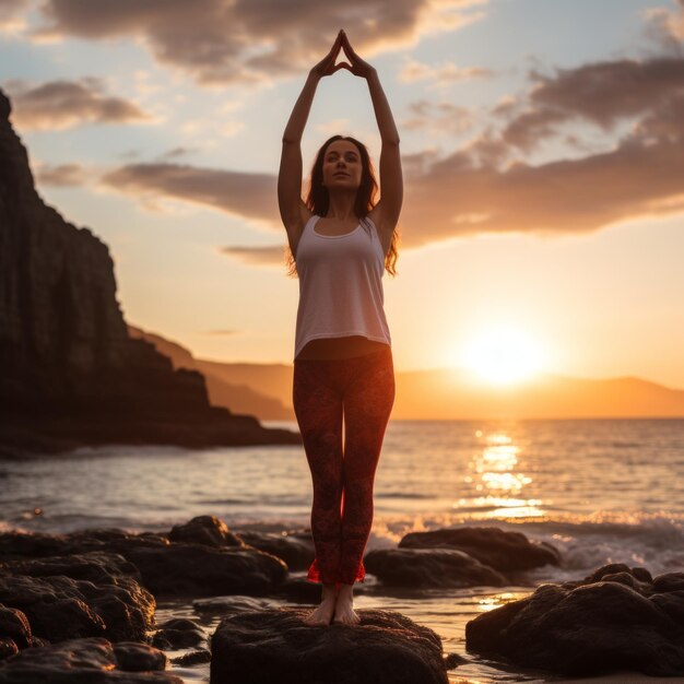 Frau in weißem Hemd und roten Hosen macht bei Sonnenuntergang Yoga am Strand