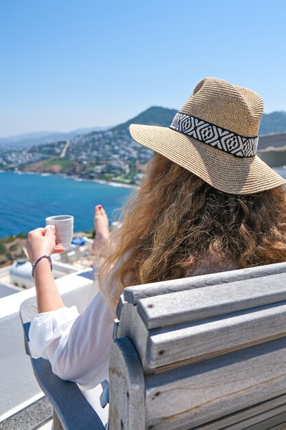 Frau in weißem Kleid und Strohhut und Kaffeetasse Sea View.