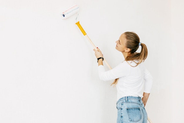 Frau in weißen Kleidern malt die Wände in ihrem großen und hellen Zimmer