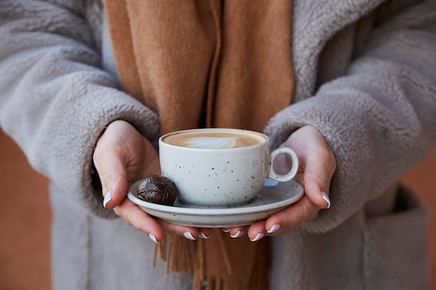 Foto frau in winterkleidung hält cappuccino mit süßigkeiten im freien frühstück auf der terrasse