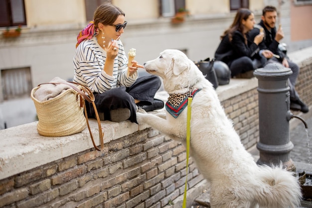 Frau isst Eis, während sie mit Hund auf einer Straße im Freien sitzt