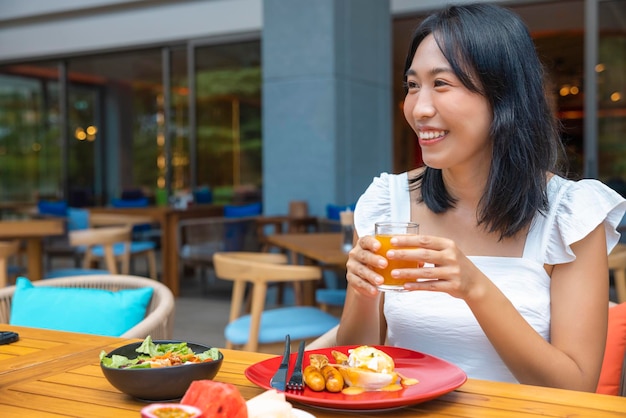 Frau isst Frühstück Egg Benedict Früchte wie Wassermelone, Papaya, Melone, Passionsfrucht, Orangensaft und Kaffee auf einem grauen Tischset