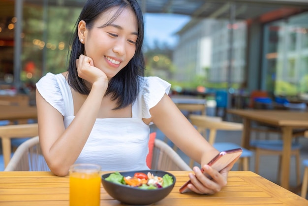 Frau isst Frühstück und spielt Smartphone Früchte wie Wassermelone, Papaya, Melone, Maracuja