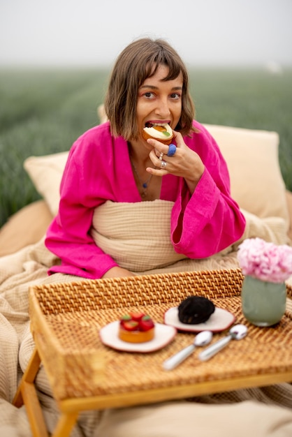 Frau isst Süßigkeiten, während sie auf dem Feld im Freien aufwacht