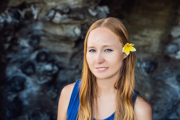 Frau ist ein Tourist in Bali. Das Ritual der Waschung mit Weihwasser und Prikleeli-Reis auf der Stirn und das Blumenohr.