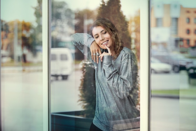 Frau junger Erwachsener schön vor dem Fenster mit Blick auf die Straßen der Stadt durch das Glas